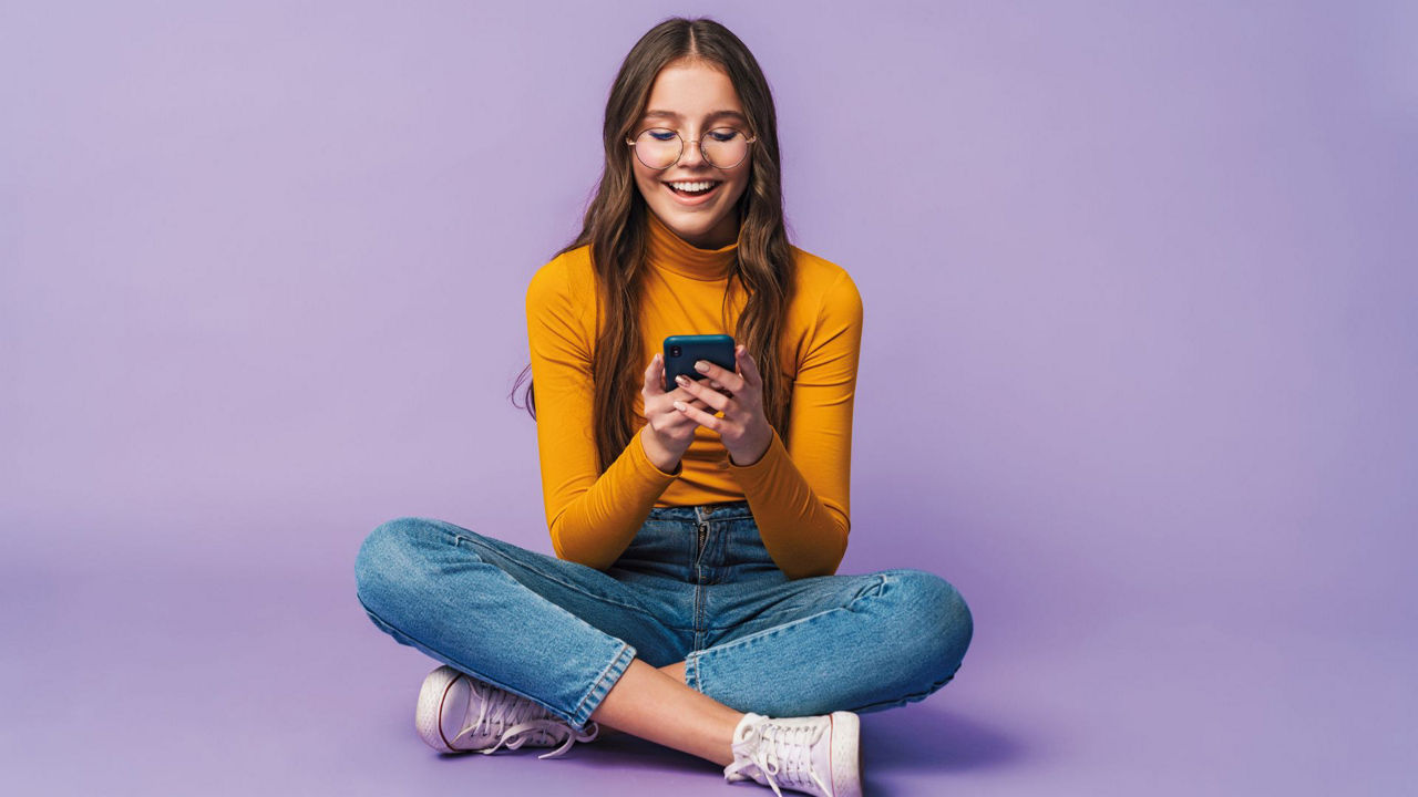 Ein Teenager sitzt im Schneidersitz und schaut auf ein Smartphone