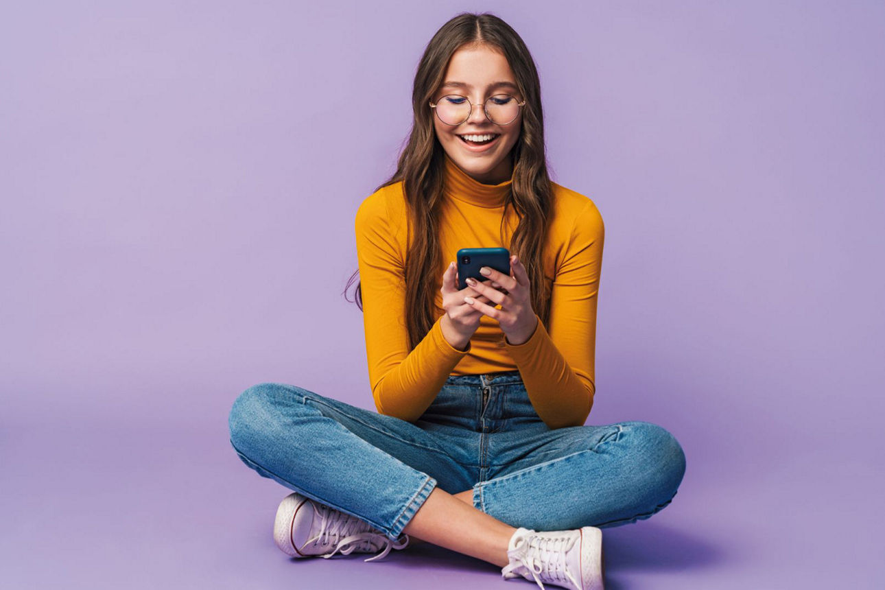 Ein Teenager sitzt im Schneidersitz und schaut auf ein Smartphone