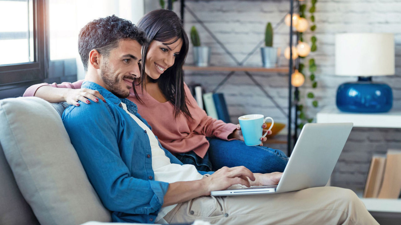 Junges Paar sitzt auf der Couch und schaut auf einen Laptop