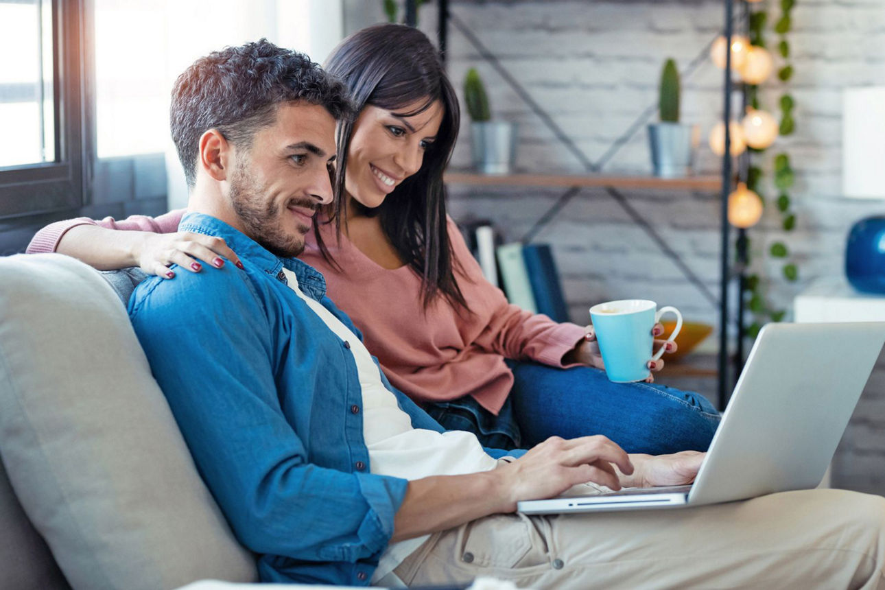 Junges Paar sitzt auf der Couch und schaut auf einen Laptop