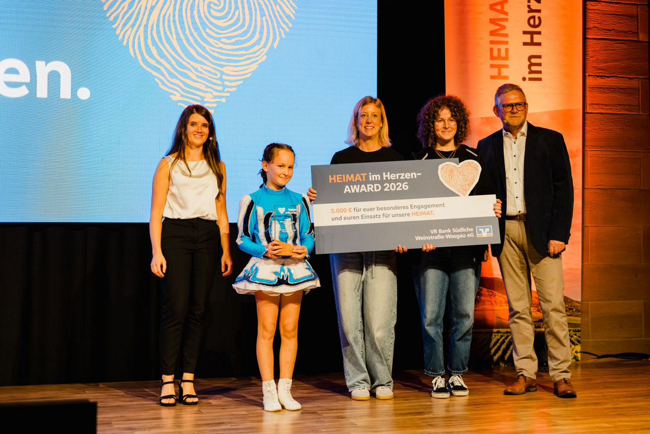 Preisverleihung auf einer Bühne mit Award-Trophäe und symbolischem Scheck zum „HEIMAT im Herzen Award 2026“