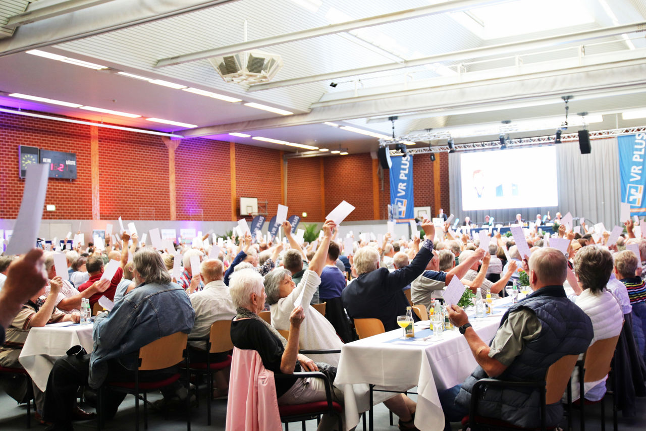 Eine große Gruppe von Menschen ist in einer hell erleuchteten Halle versammelt.