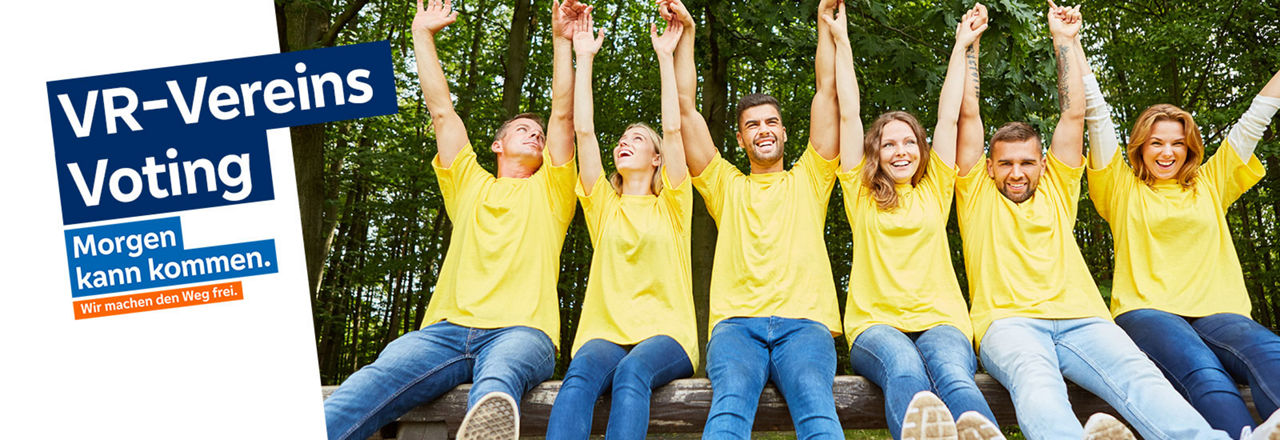 Sechs Erwachsene in gelben Shirts jubeln, in dem sie ihre Hände in die Luft strecken. Sie sitzen nebeneinander auf einem Baumstamm.