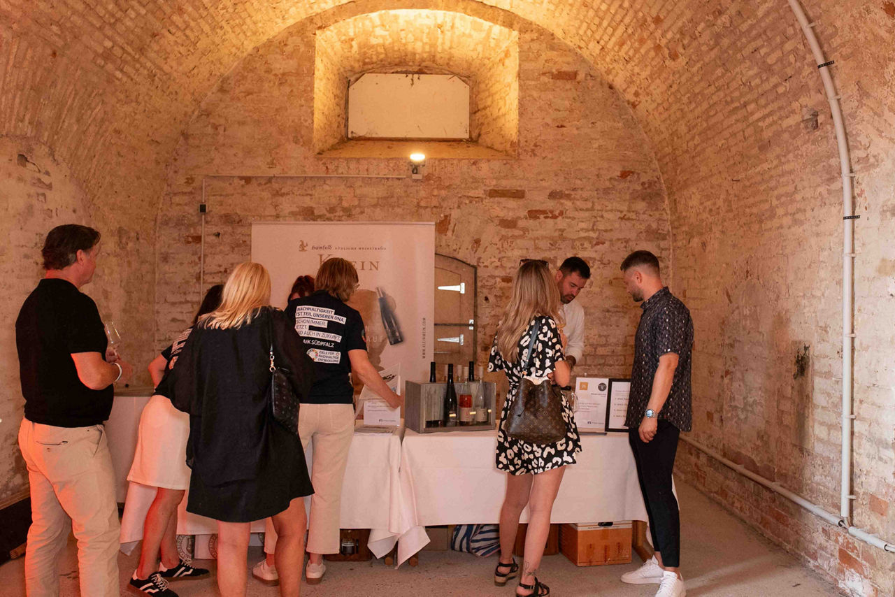 Eine Gruppe von Menschen verkostet Wein an einem Winzerstand im Gewölbeambiente des Grabenwehrgebäude der Festungsanlage.