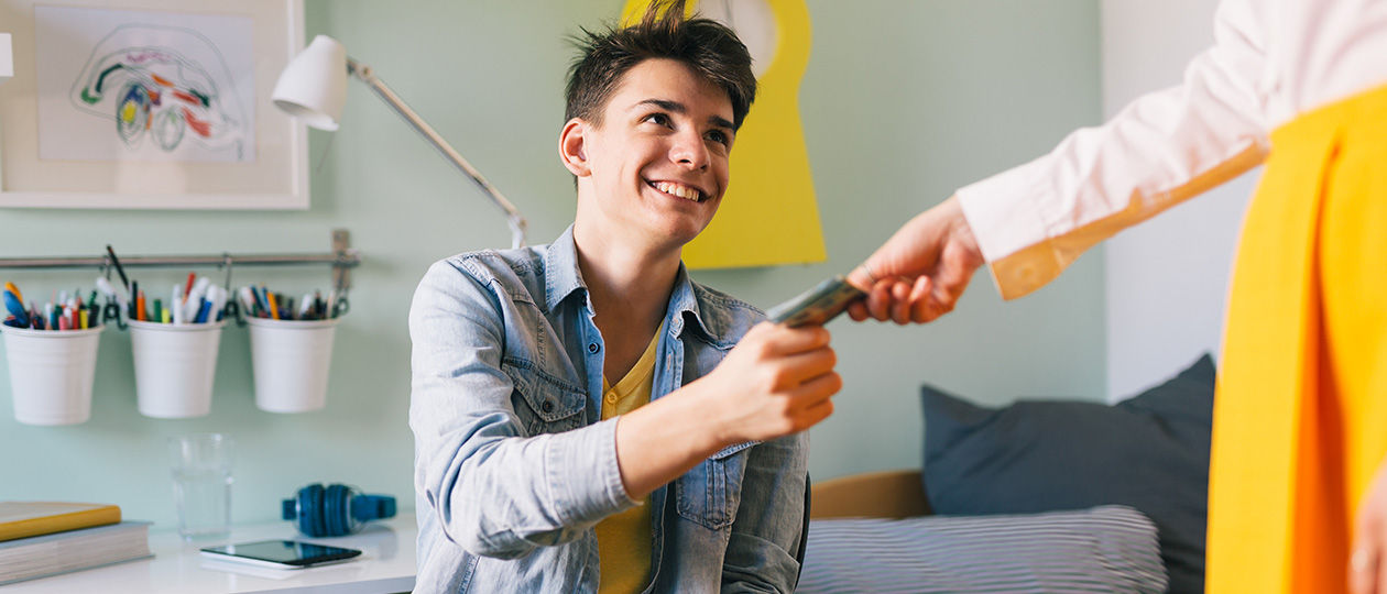 ein lächelnder Teenager bekommt Taschengeld überreicht