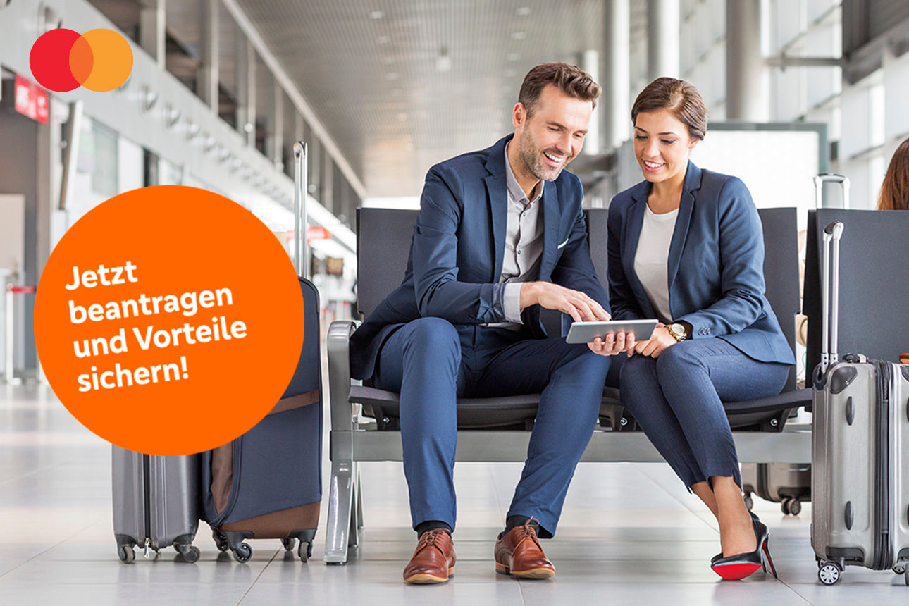 Mann und Frau blicken sitzend auf ein Tablet am Flughafen