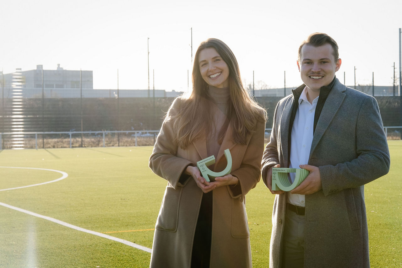 VR Bank München Land eG Mitarbeitende Lena Meinzer und Quirin Altinger mit dem Nachhaltigkeitspreis auf dem Fußballplatz