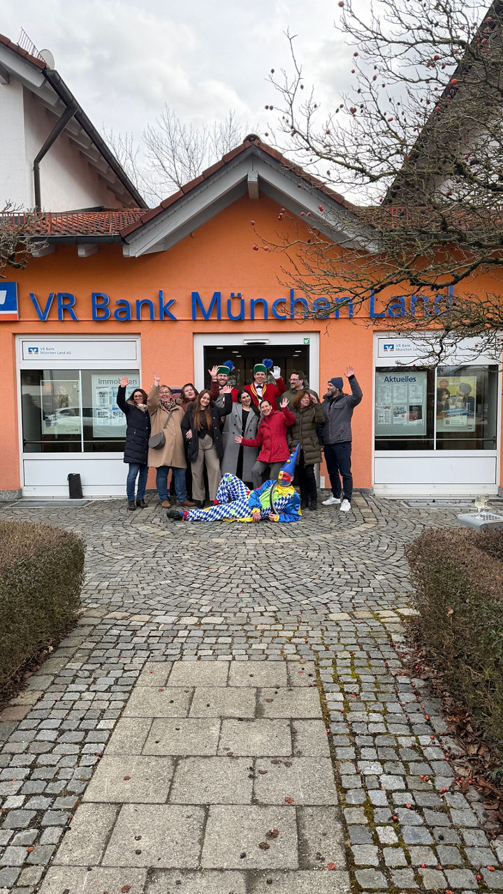 Eine Gruppe freut sich vor der Filiale VR Bank München Land eG Heimstetten