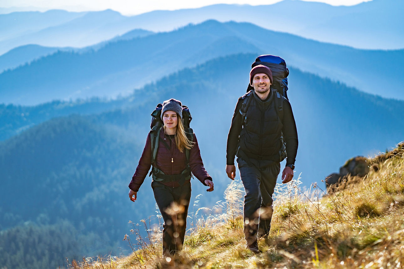 Frau und Mann wandern auf einem Berg, im Hintergrund sind weitere Berge