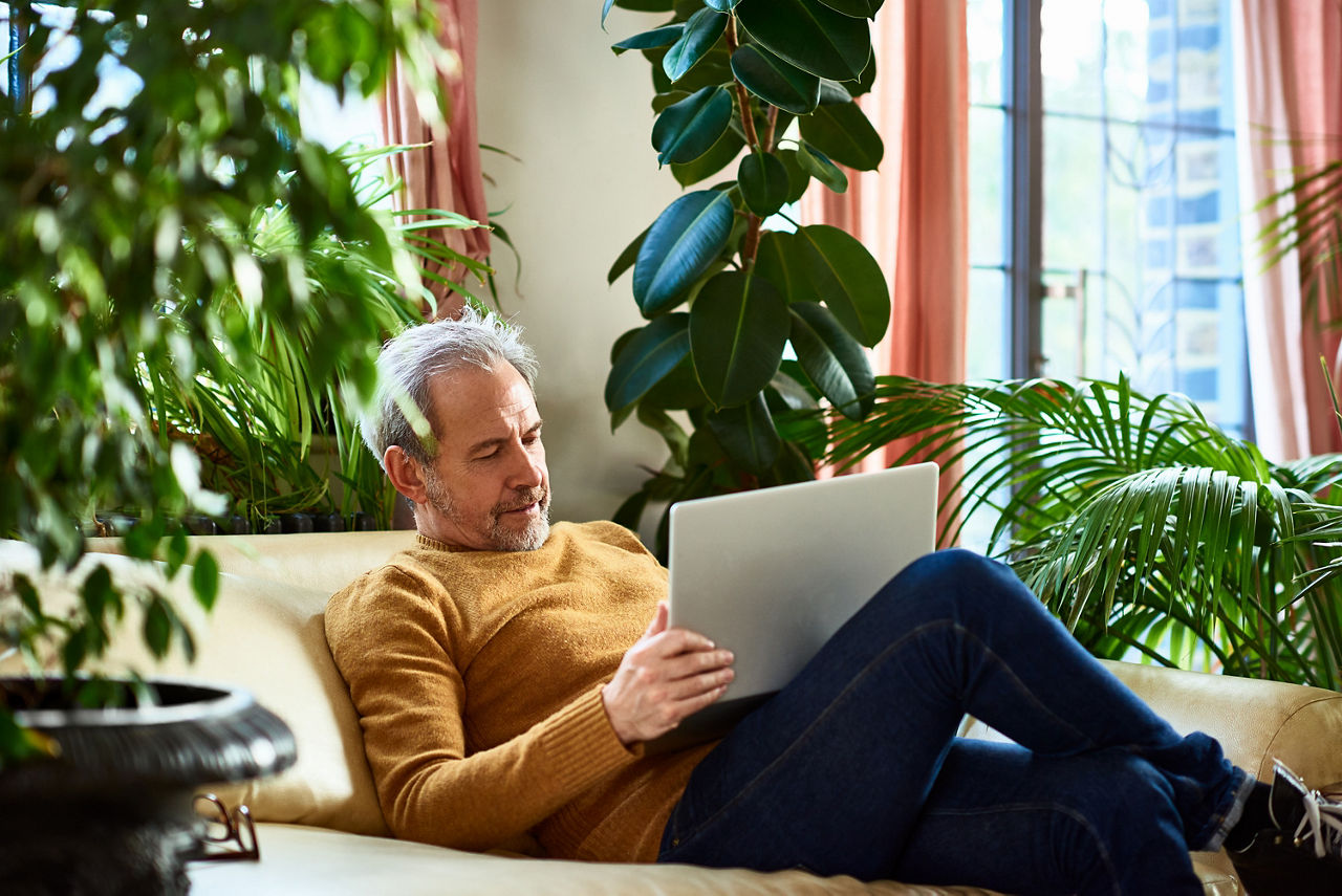 Mann sitzt auf der Couch und hat seinen Laptop auf dem Schoß, er schaut konzentriert