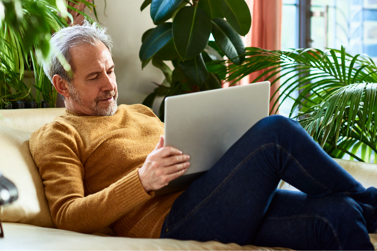 Mann sitzt auf der Couch und hat seinen Laptop auf dem Schoß, er schaut konzentriert