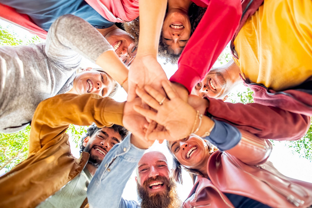 Menschengruppe legt Hände in der Mitte zusammen für Zusammenhalt & Teamwork 