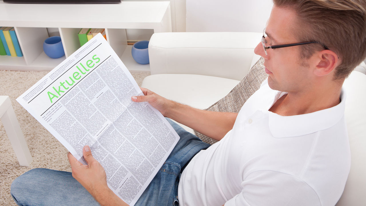 Ein Mann sitzt entspannt auf einem Sofa und liest Zeitung