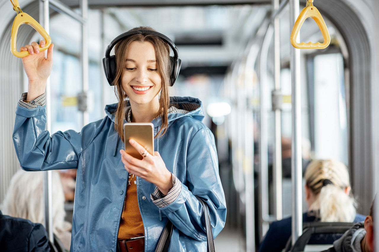 Junge Frau mit Kopfhörer steht im Bus und schaut auf ihr Handy