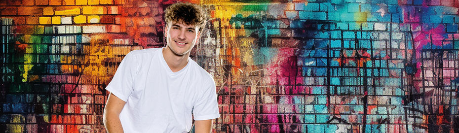 Junger Mann in weißem T-Shirt steht vor einer bunt besprühten Graffiti-Wand und lächelt.