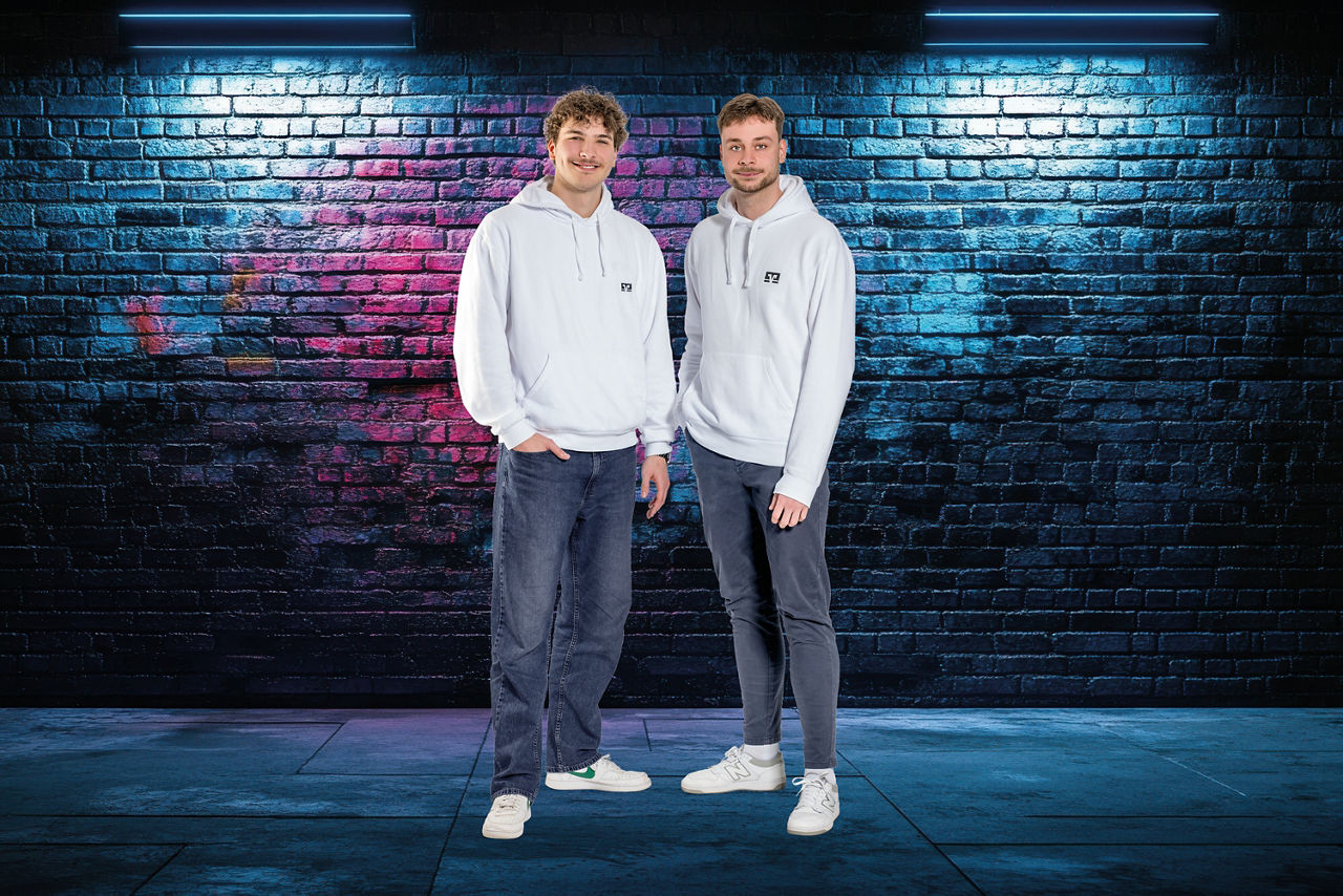 Lukas Wetter, MoneyMate und Felix Klingelhöfer MoneyMate stehen in weißem Hoddi vor einer Bachsteinwand
