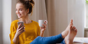 Frau mit gelben Shirt und Handy in der Hand am Kaffee trinken