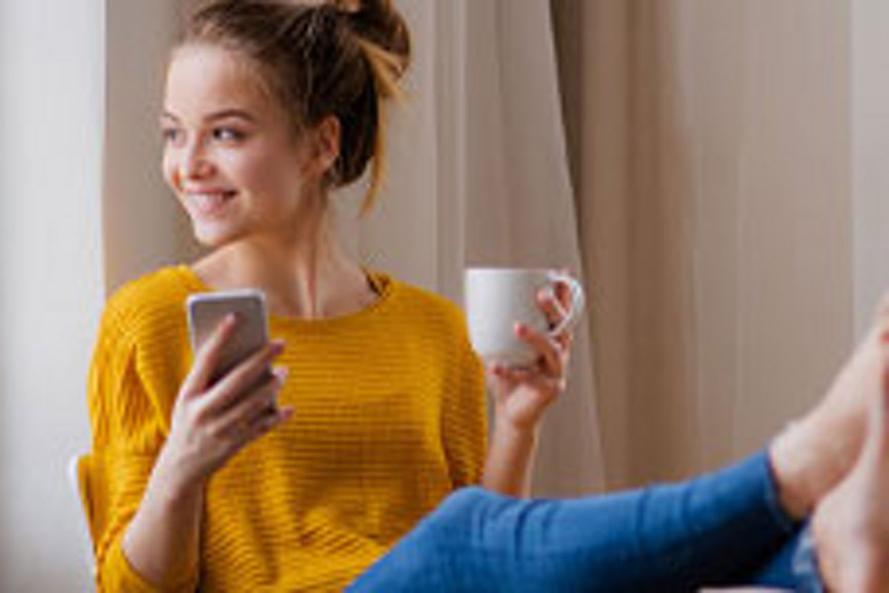 Frau mit gelben Shirt und Handy in der Hand am Kaffee trinken