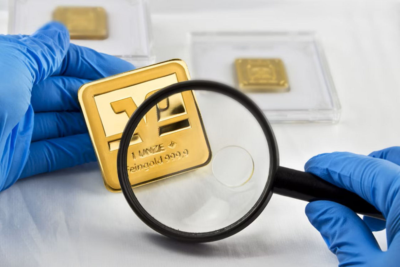 Blaue Handschuhe halten eine Lupe über einem Goldbarren in Schutzverpackung; weitere Goldbarren im Hintergrund
