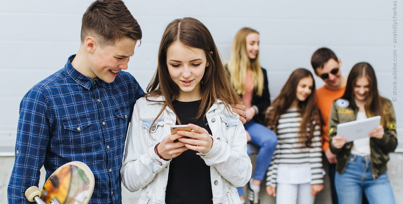 Jugendliche stehen zusammen und schauen auf ein Smartphone