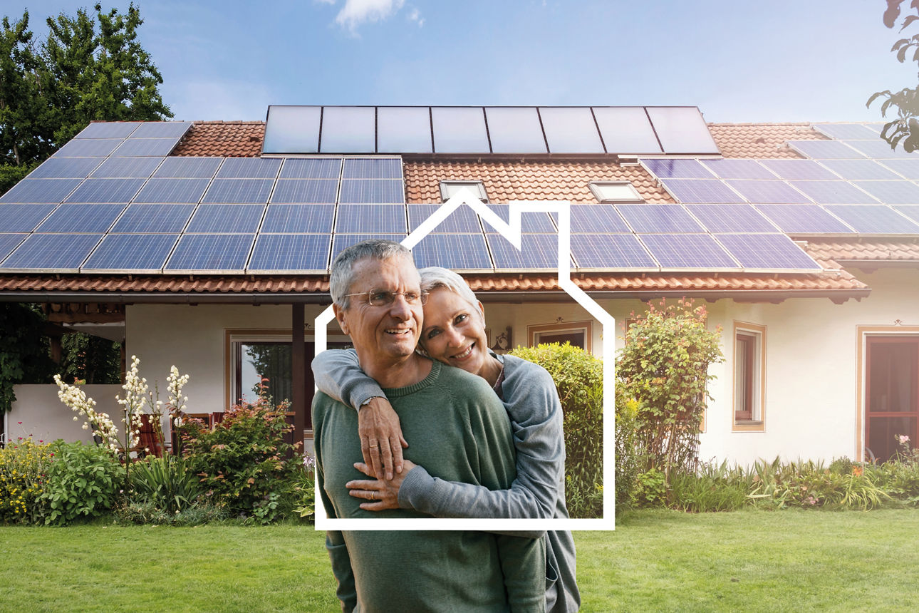 Ein Paar liegt sich glücklich in den Armen, im Hintergrund ist ihr neues Haus zu sehen