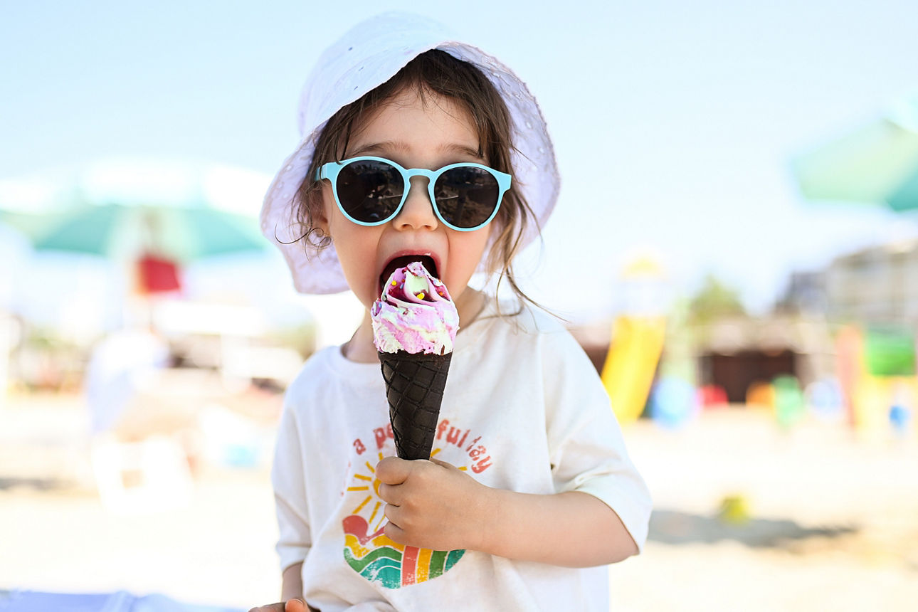 Kleines Mädchen mit Sonnenbrille am Strand schleckt an einem Eis