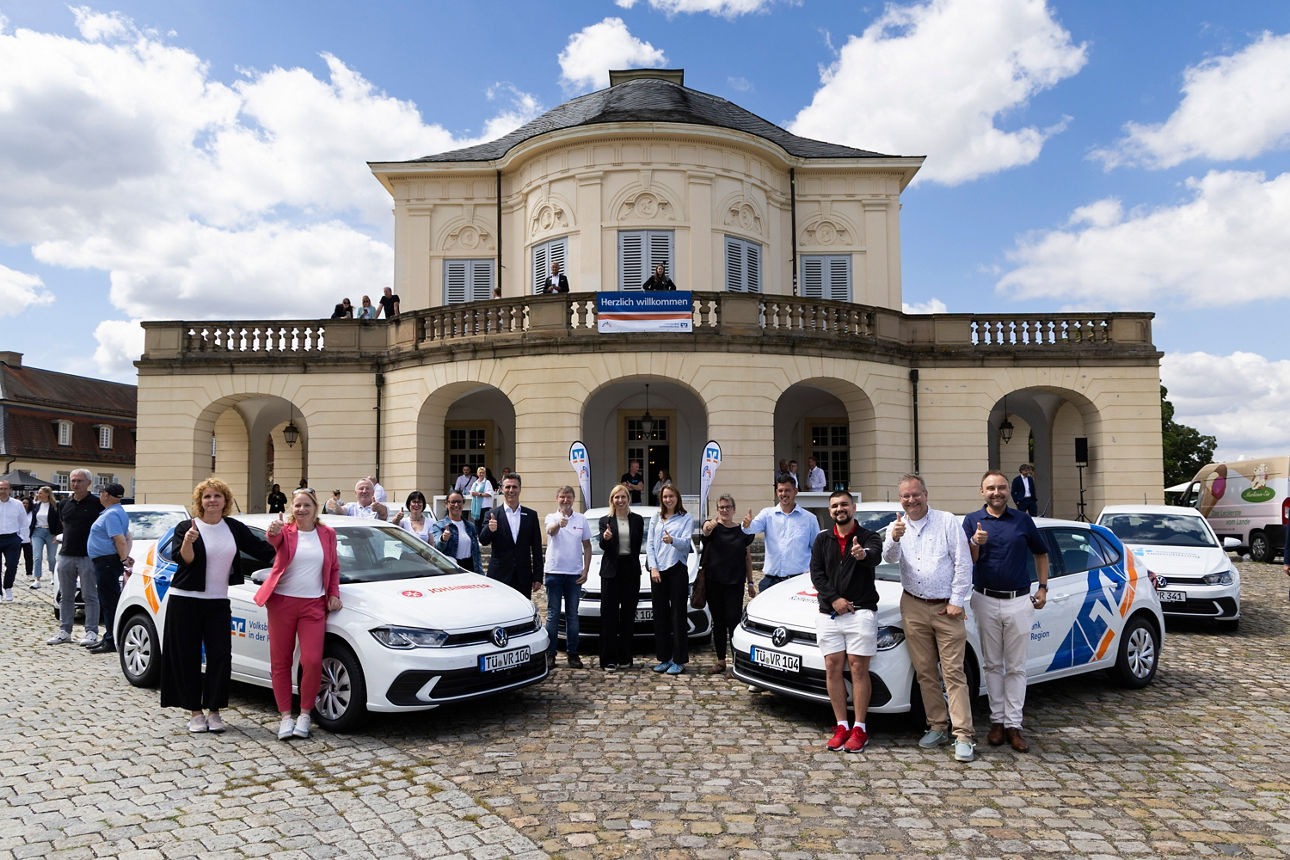 Personen stehen vor Schloss neben mehreren Autos und halten Daumen hoch