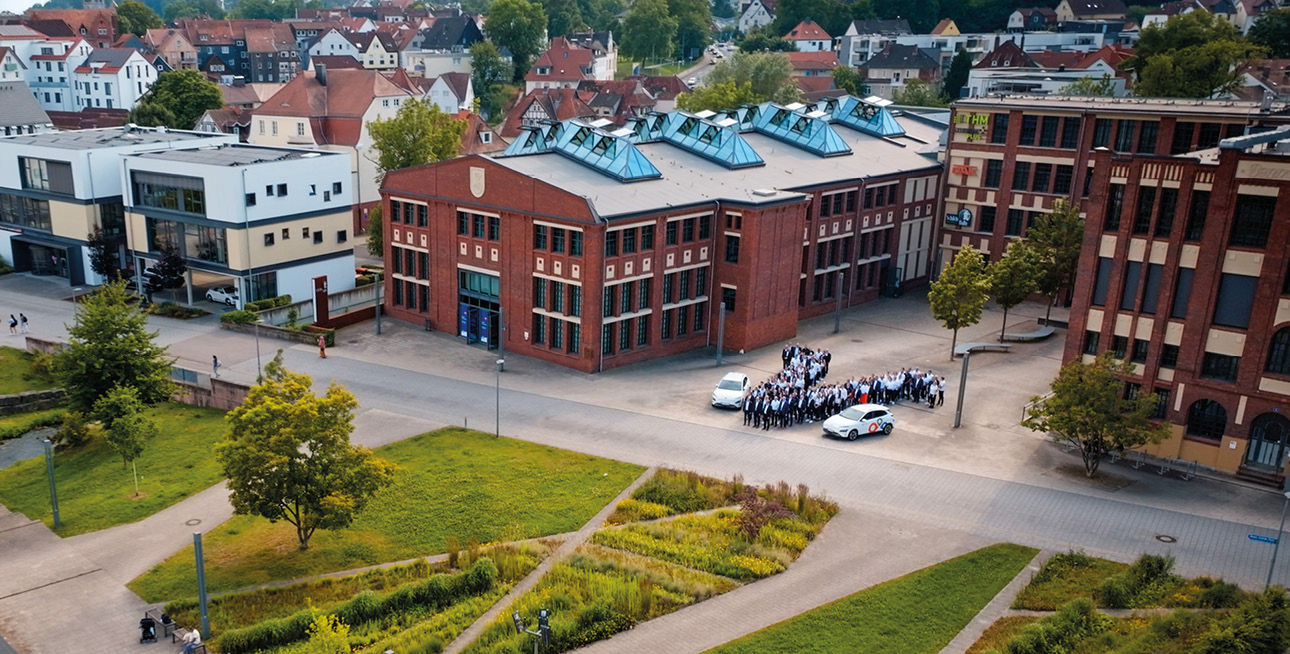 Stadtansicht von Bad Hersfeld mit der Schildehalle und einem V aus den Mitarbeitenden der Bank