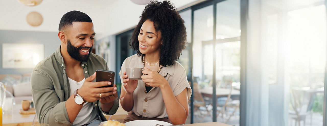 Ein Pärchen trinkt Kaffee und schauen sich zusammen auf einem Handy etwas an