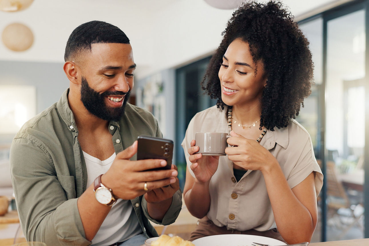 Ein Pärchen trinkt Kaffee und schauen sich zusammen auf einem Handy etwas an