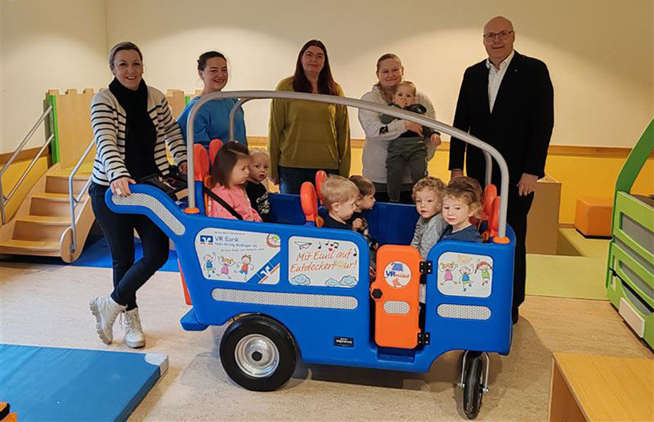 Das Bild zeigt den VRmobil Kinderbus für die Kita St. Johannes. Der bunte Bus steht in der Einrichtung, umgeben von fröhlichen Kindern und Erziehern.