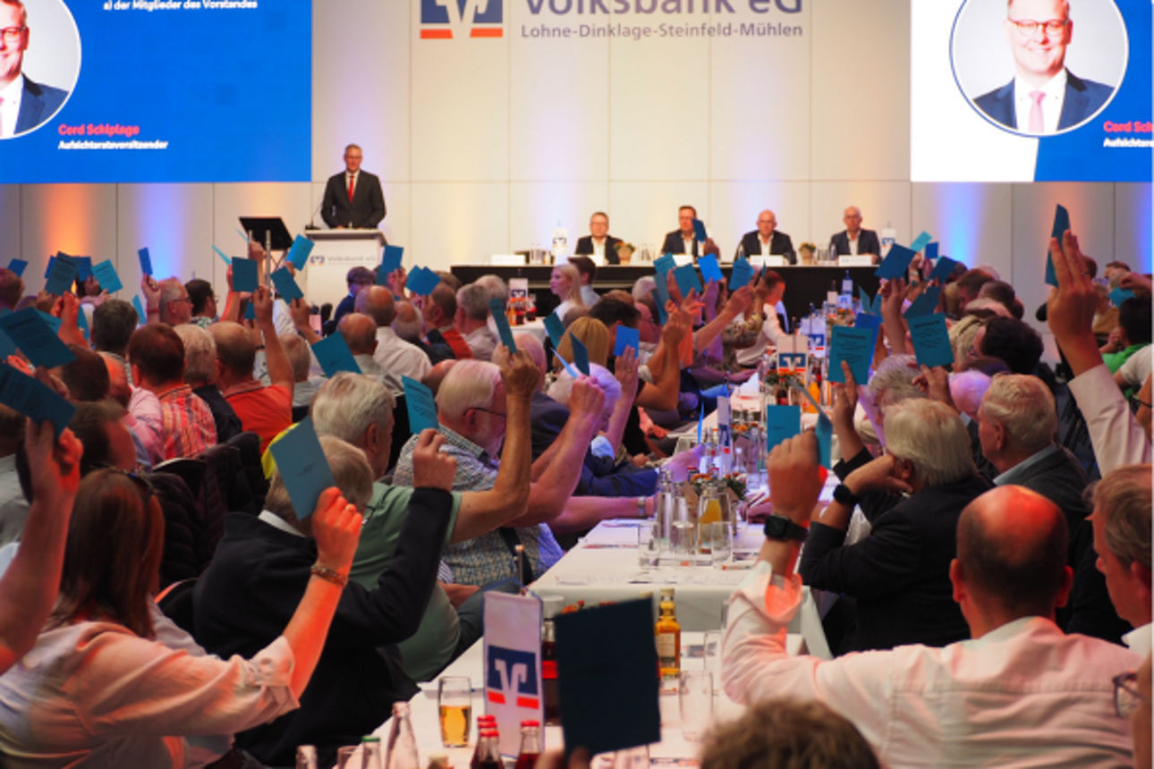 Auf einer Versammlung halten die Besucher blaue Stimmzettel hoch.