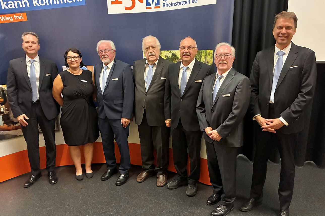 Eine Gruppe von Menschen, die vor einer Firmenkulisse der Spar- und Kreditbank Rheinstetten eG in einer Reihe stehen.