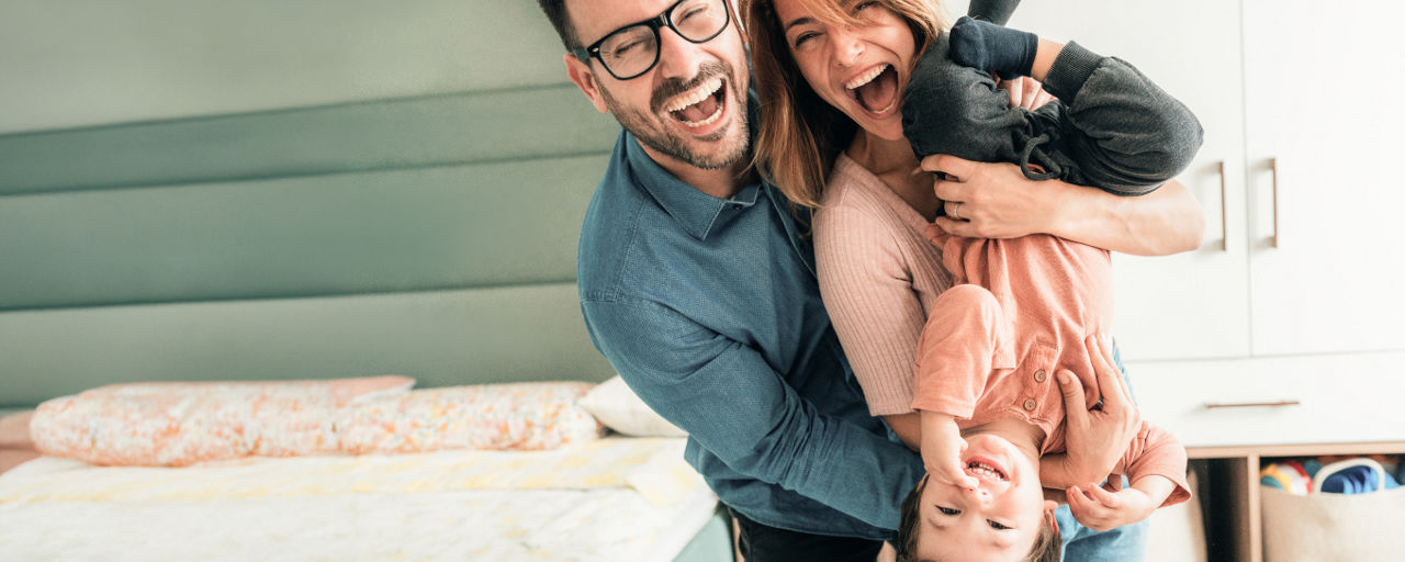 Mann und Frau mit Kind stehen lachend in ihrem Zuhause