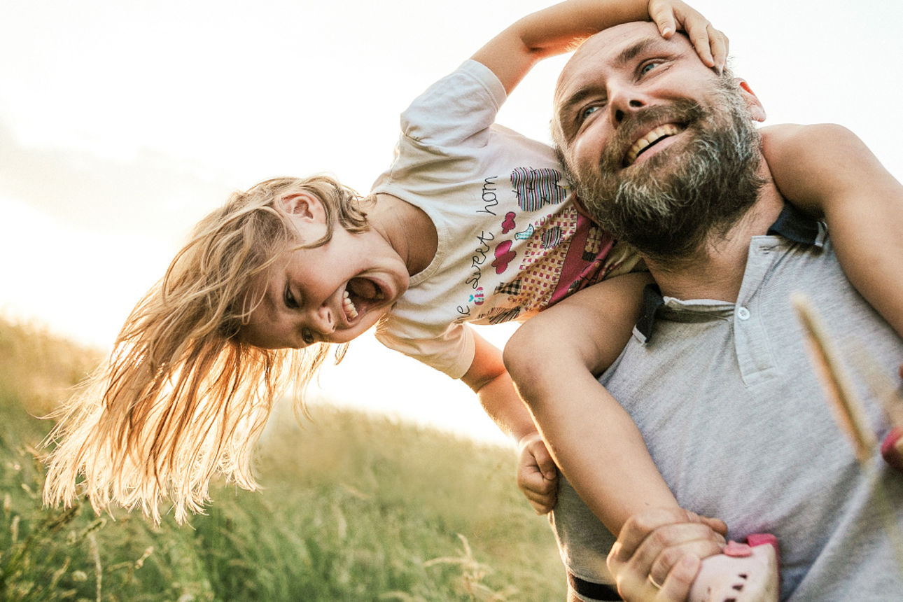 Mann trägt ein Kind Huckepack über einen Wiese
