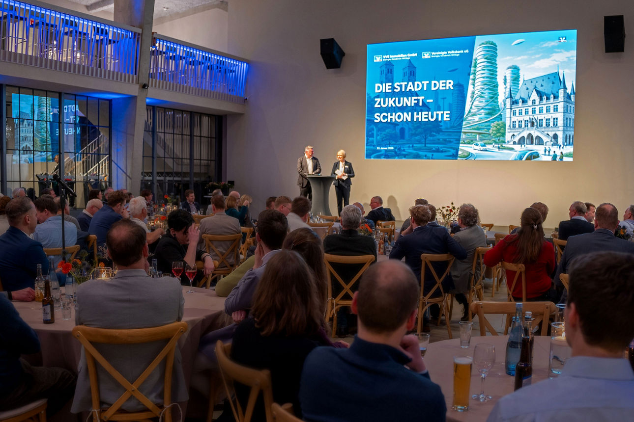 Große Veranstaltung mit Publikum, Bühne und Präsentation über die Zukunft der Stadt in einer modernen Halle.