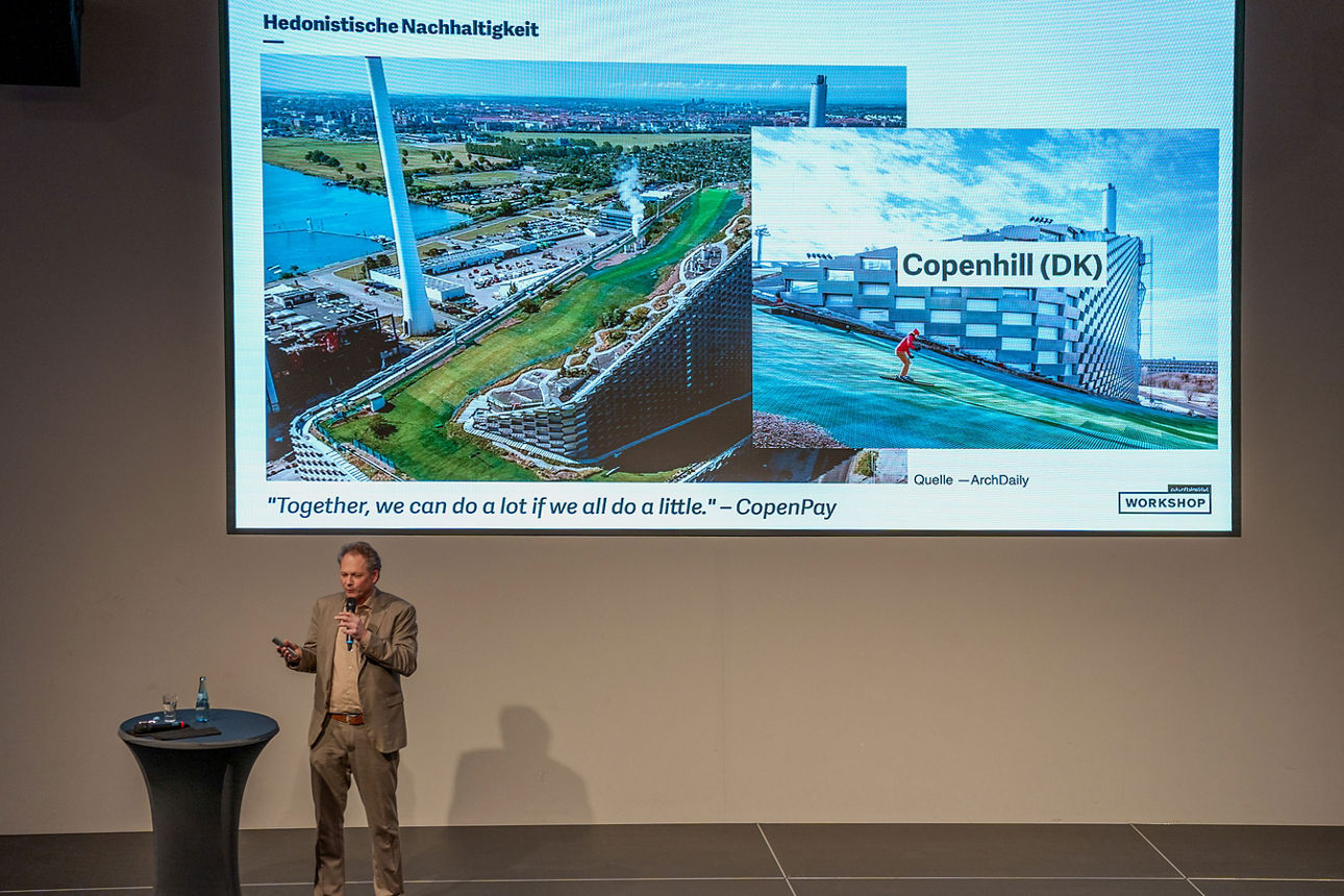 Ein Mann hält einen Vortrag vor einer Leinwand, die das Projekt „CopenHill“ zum Thema hedonistische Nachhaltigkeit zeigt.
