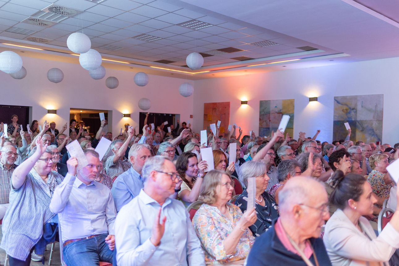 Vertreter der Vertreterversammlung heben den Arm zu Abstimmung.