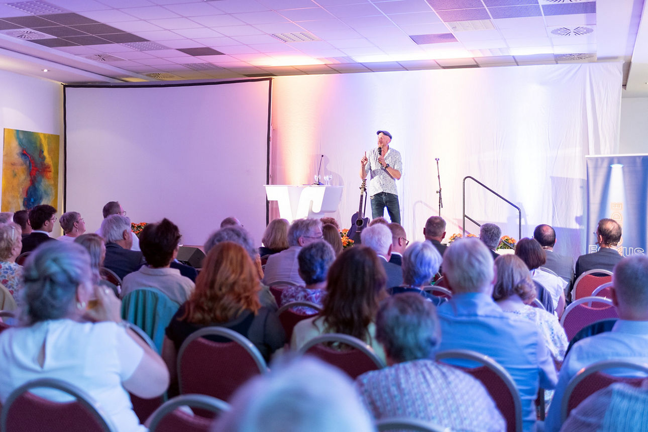 Martin Schopps auf der Bühne. Im Vordergrund kann man das Publikum erkennen.