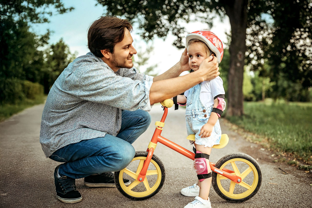 Vater setzt seiner kleiner Tochter einen Fahrradhelm auf