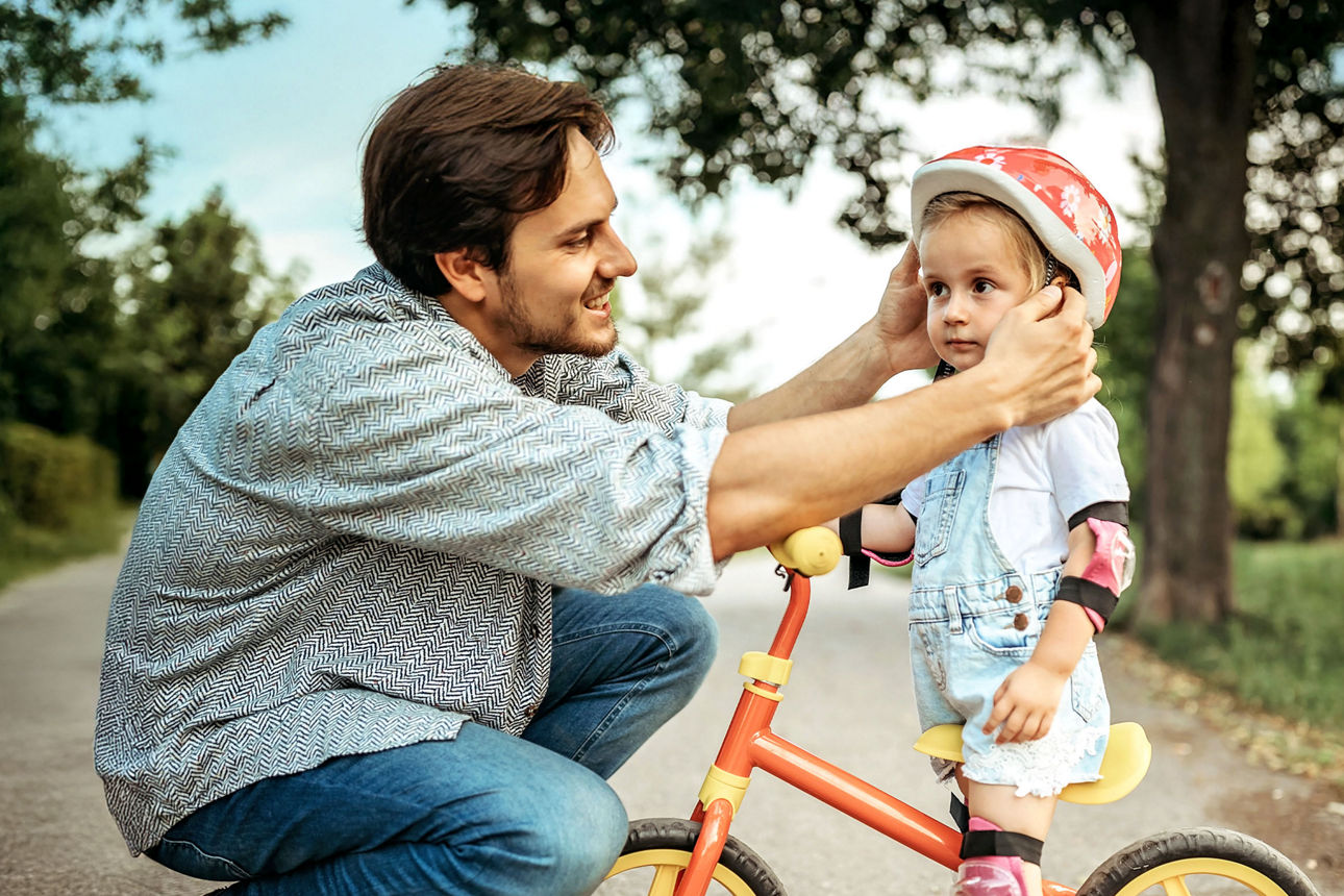Vater setzt seiner kleiner Tochter einen Fahrradhelm auf