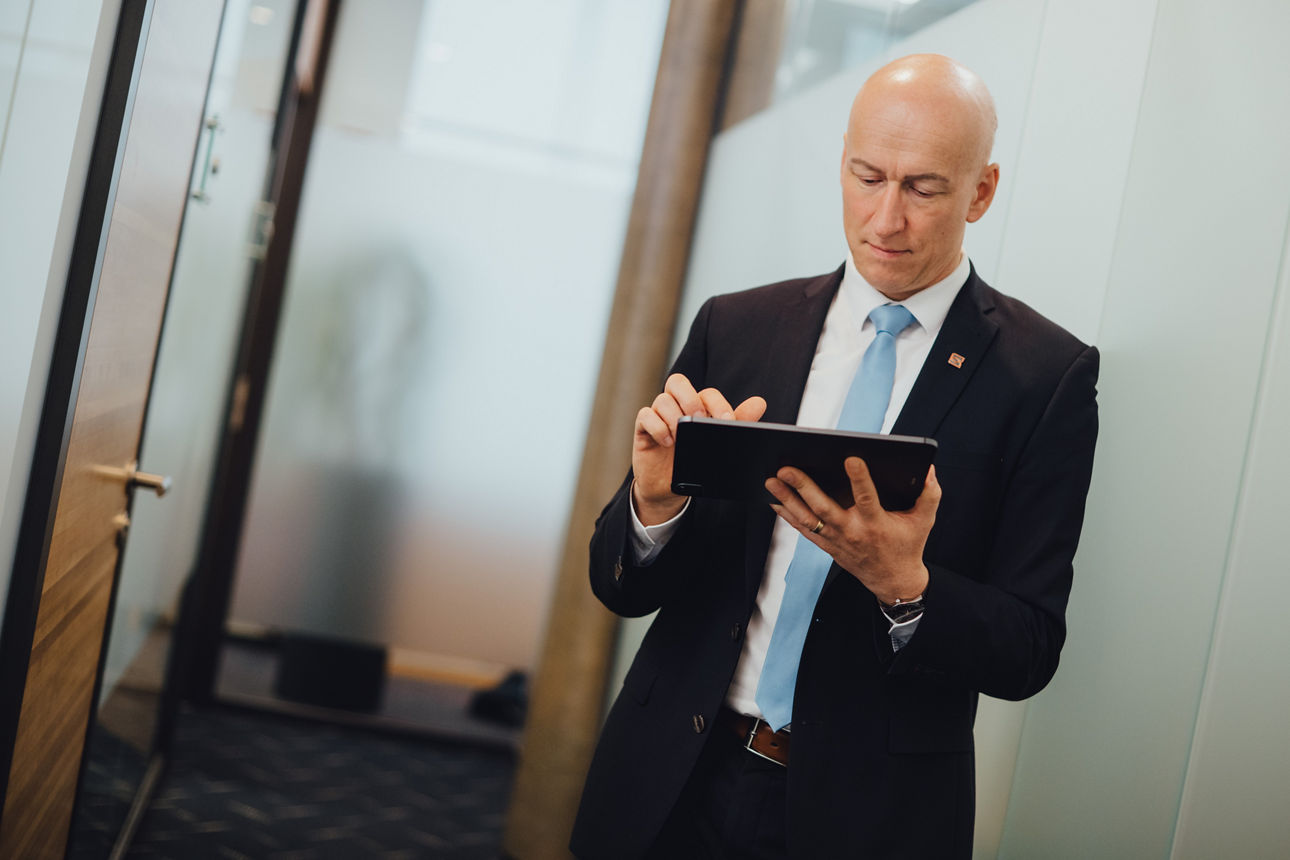 Ein Mitarbeiter steht im Büro und schaut etwas auf seinem Tablet nach