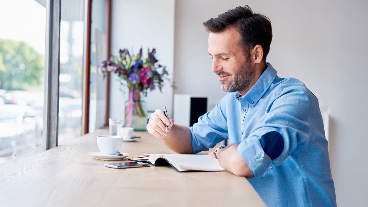 Ein junger Mann sitzt an einem Tisch mit einer Tasse Kaffee und liest Zeitung
