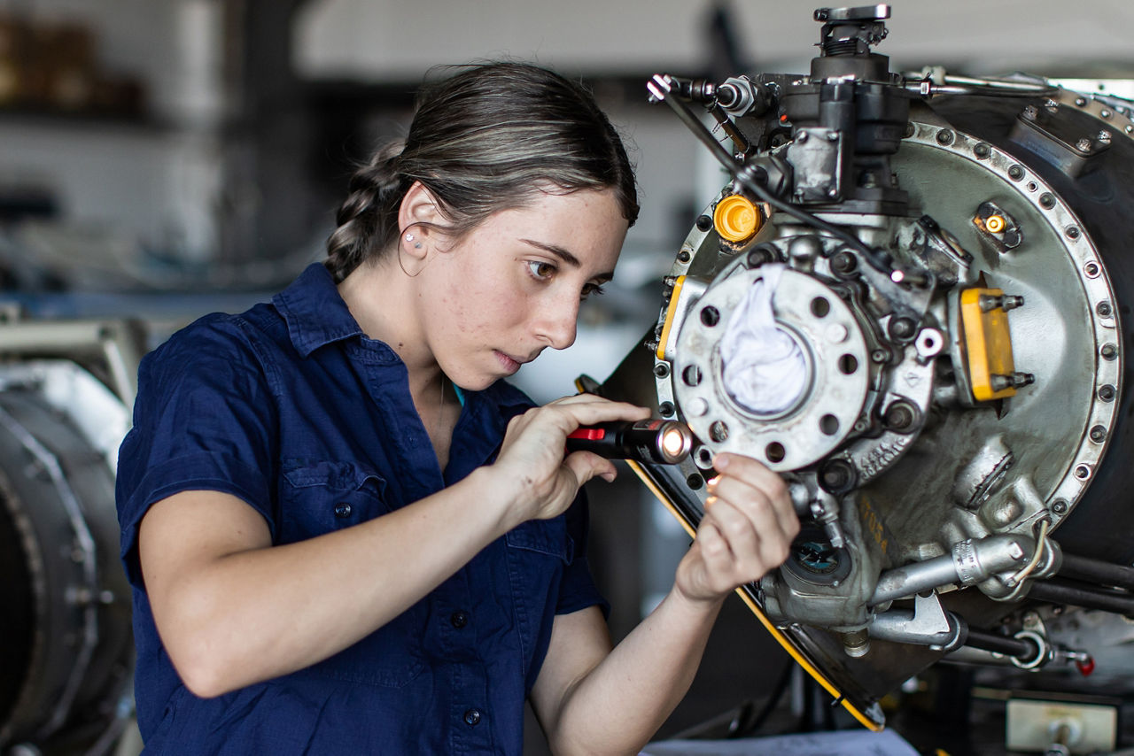 Eine junge Mechanikerin untersucht einen Motor mit der Taschenlampe