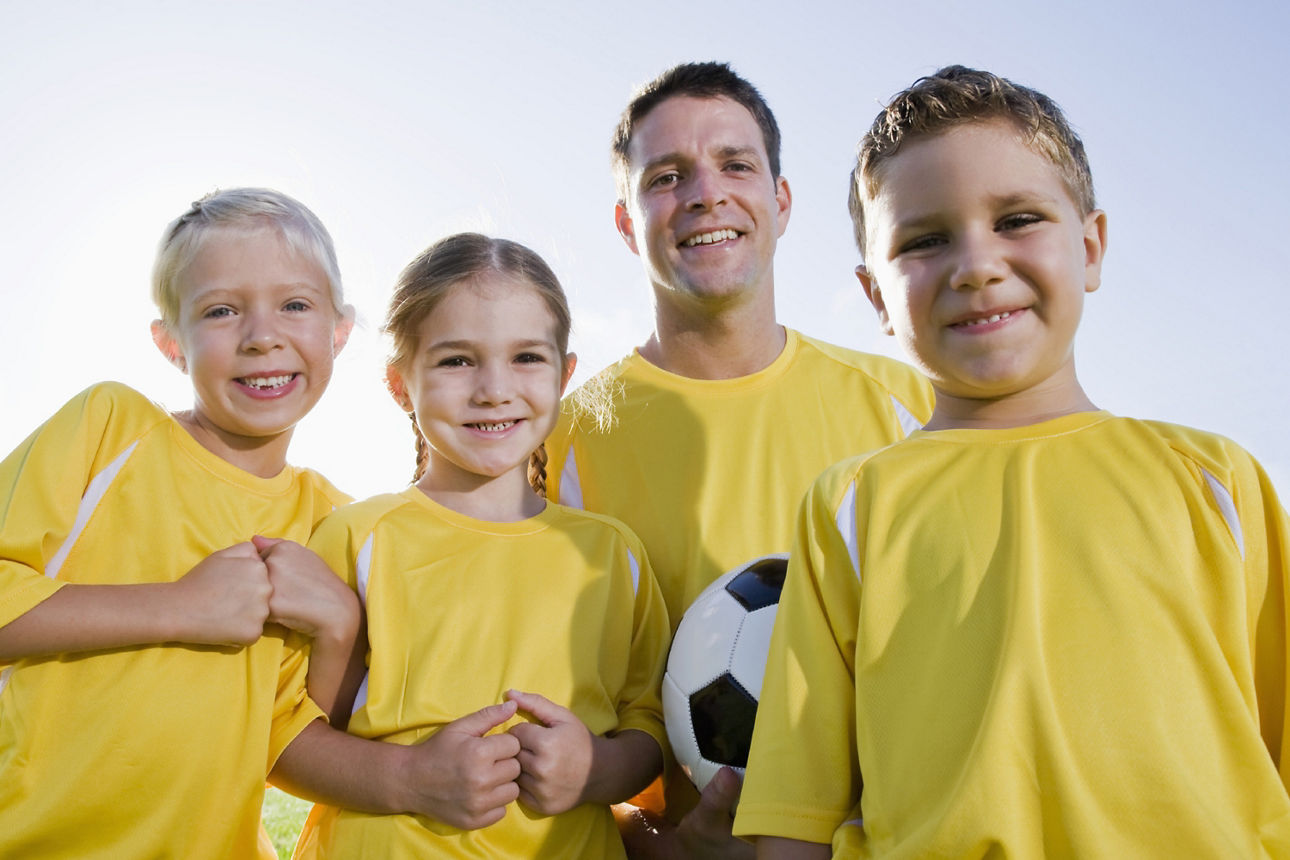 Trainer mit 3 Kindern im Vereinstrikot und Fußball