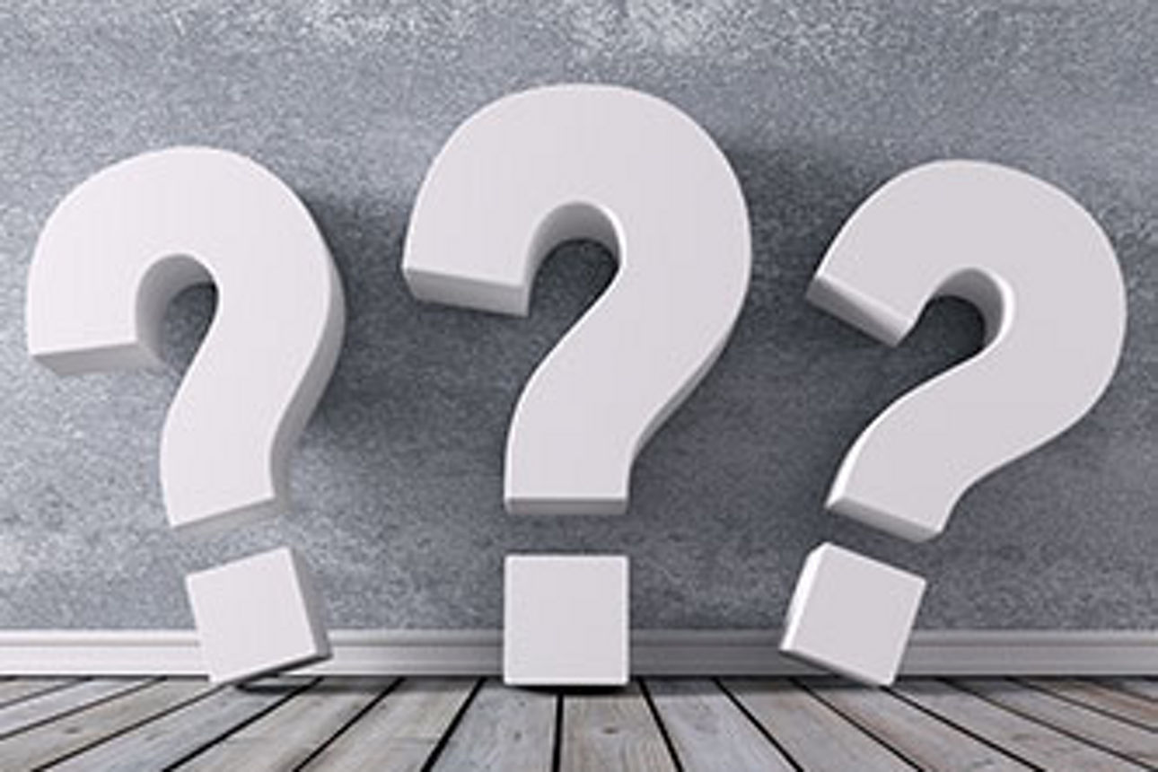 Auf dem Bild sind drei weiße Fragezeichen in einem Raum mit grauem Holzboden und grauer Wand zu sehen.