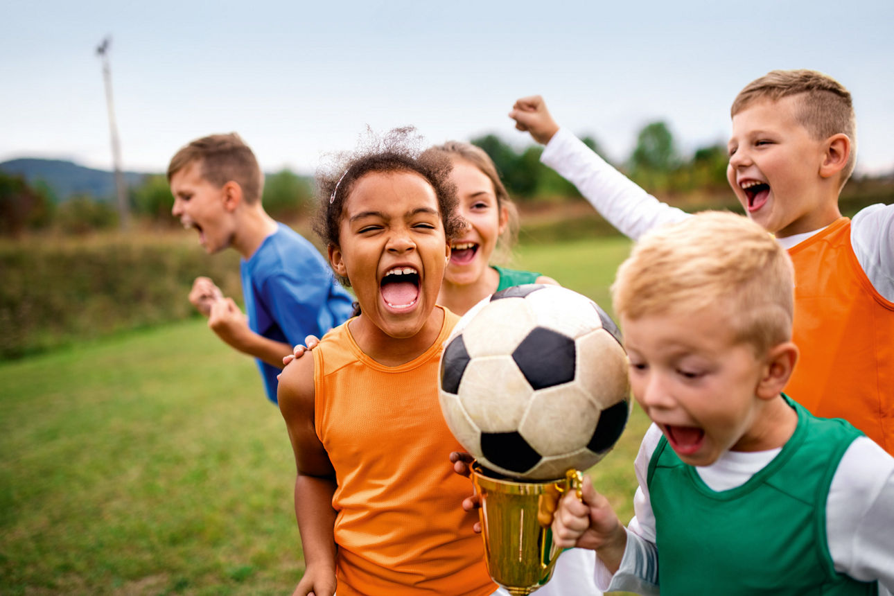 Kinder spielen Fußball und jubeln dabei