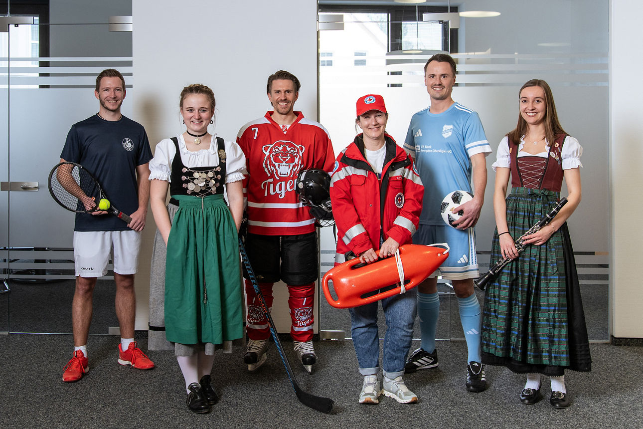 6 Mitarbeiter tragen die typischen Trikots, Tracht und Kleidung der Vereine, in denen sie sich engagieren