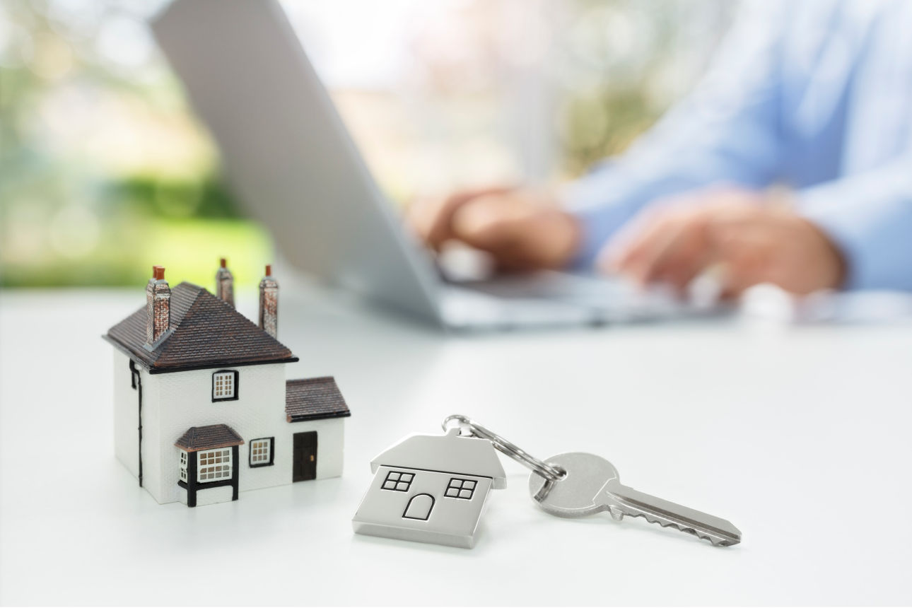 Ein kleines Deko-Haus und ein Hausschlüssel liegen auf einem Tisch.