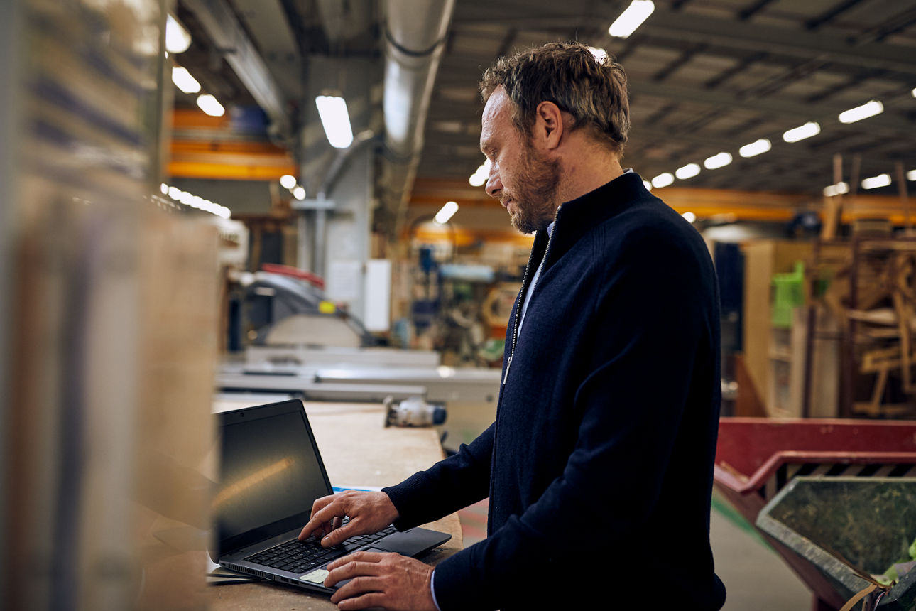 Ein Mann in einer Lagerhalle arbeitet an einem Laptop.